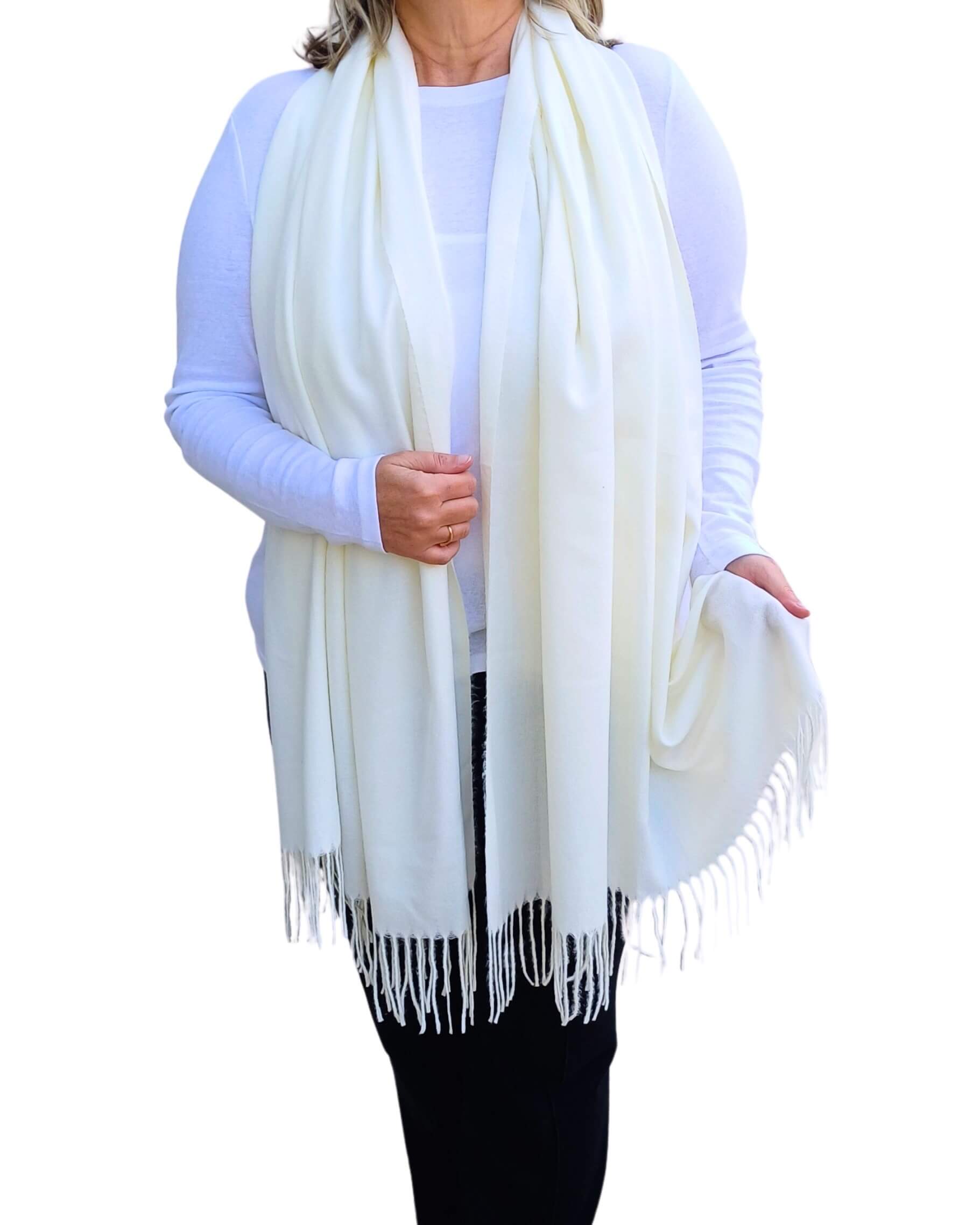 Aurora's Array: Woman models a soft, warm ivory cream wool blend scarf with fringed edges, draped around her neck and shoulders.
