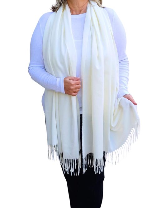 Aurora's Array: Woman models a soft, warm ivory cream wool blend scarf with fringed edges, draped around her neck and shoulders.