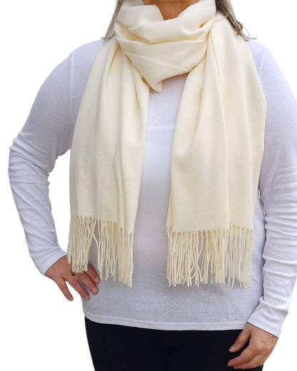 Aurora's Array: Woman models a soft, warm off-white cream wool blend scarf with fringed edges, draped around her neck and shoulders.