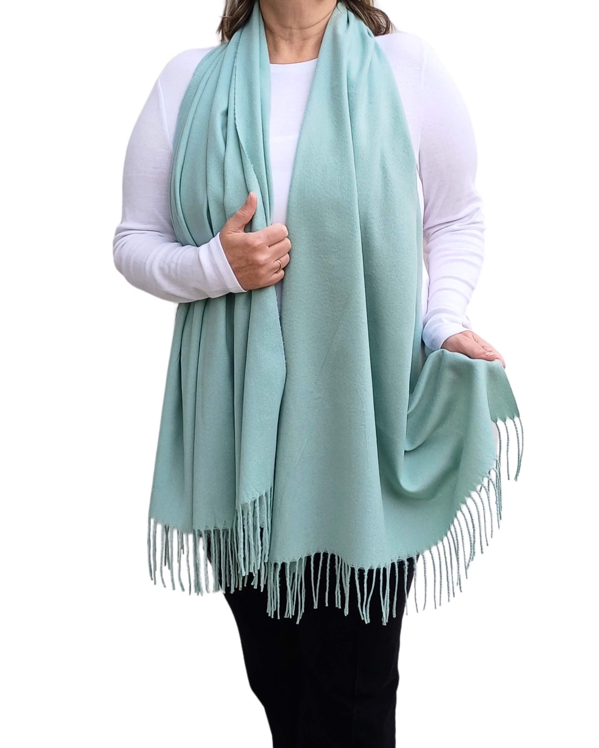 Aurora's Array: Woman models a soft, warm duckegg green wool blend scarf with fringed edges, wrapped around her neck.