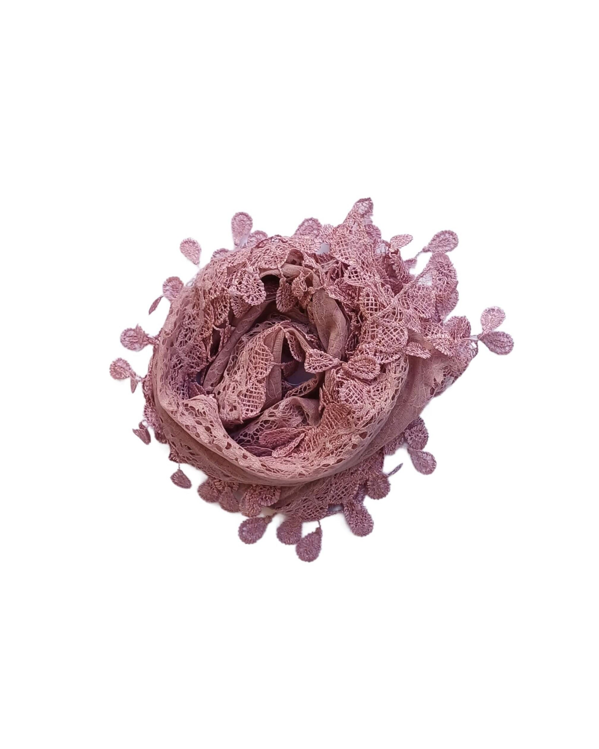 Aurora's Array: A soft mauve-coloured, light pink scarf made of delicate lace with a leaf-like pattern and fringed edges, gathered in a circular shape.