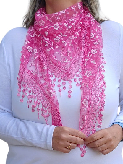  Aurora's Array Glitter Triangle Scarf: A woman wearing a bright fuchsia pink lace scarf with floral embroidery and delicate dangling lace details. The scarf is styled in a triangular shape over a plain white long-sleeve top.