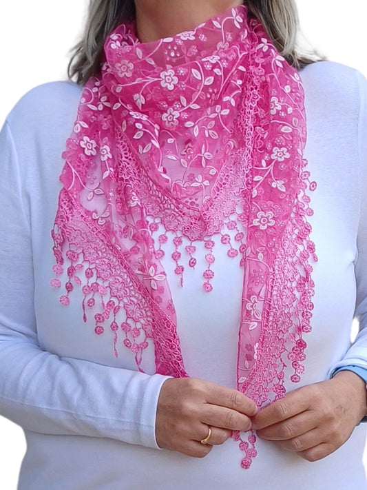  Aurora's Array Glitter Triangle Scarf: A woman wearing a bright fuchsia pink lace scarf with floral embroidery and delicate dangling lace details. The scarf is styled in a triangular shape over a plain white long-sleeve top.
