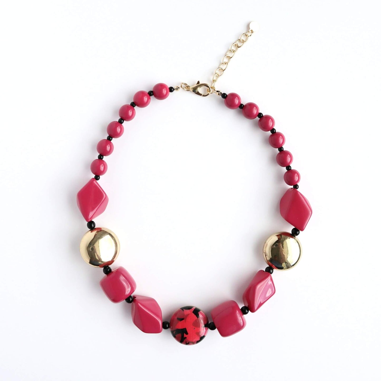 Short statement necklace with faceted fuchsia pink beads, shiny gold spheres, and a central round bead with a red and black pattern. Gold-tone clasp.