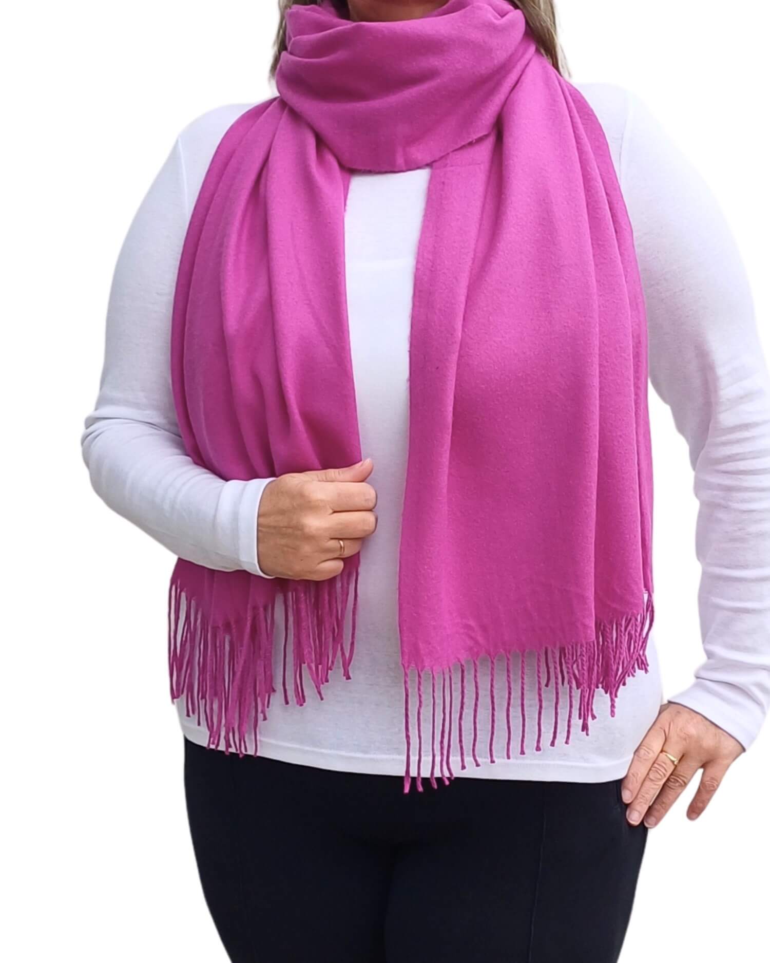 Aurora's Array: Woman models a soft, warm fuchsia pink wool blend scarf with fringed edges, wrapped around her neck.