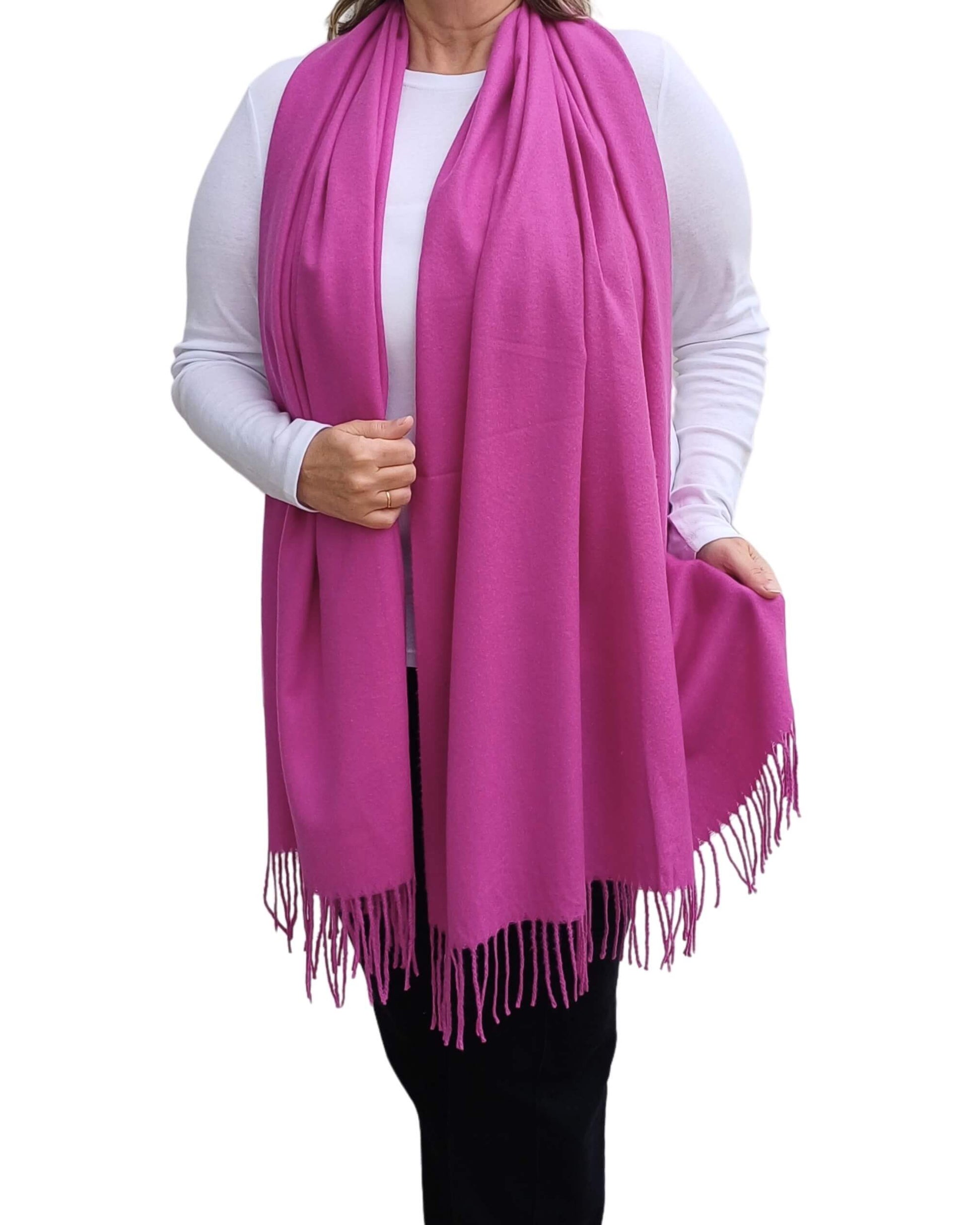 Aurora's Array: Woman models a soft, warm fuchsia pink wool blend scarf with fringed edges, wrapped around her neck.