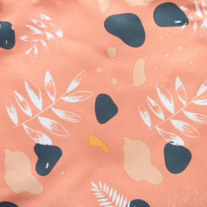 Close-up on the coral fabric of a crossbody bag, featuring a modern abstract floral and geometric pattern in navy, yellow, and white. Textured surface.