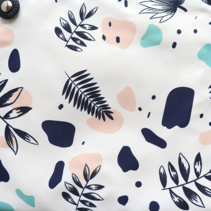 Close-up of a white crossbody bag's fabric: a modern abstract floral and geometric pattern in navy, pink, and light blue. Textured material.