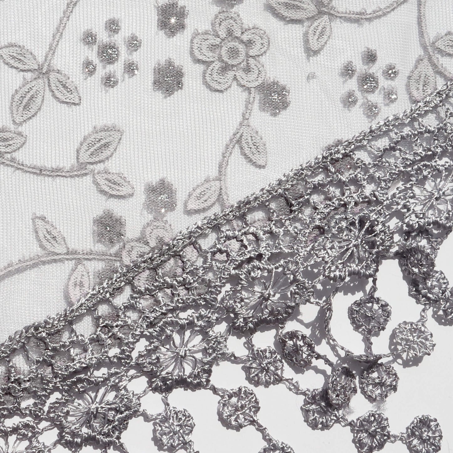 Aurora's Array Glitter Triangle Scarf with Lace & Embroidery (Close-up): A detailed close-up of a white, sheer fabric with delicate grey floral embroidery accented with subtle glitter. The edge features intricate grey lace trim with dangling embroidered d