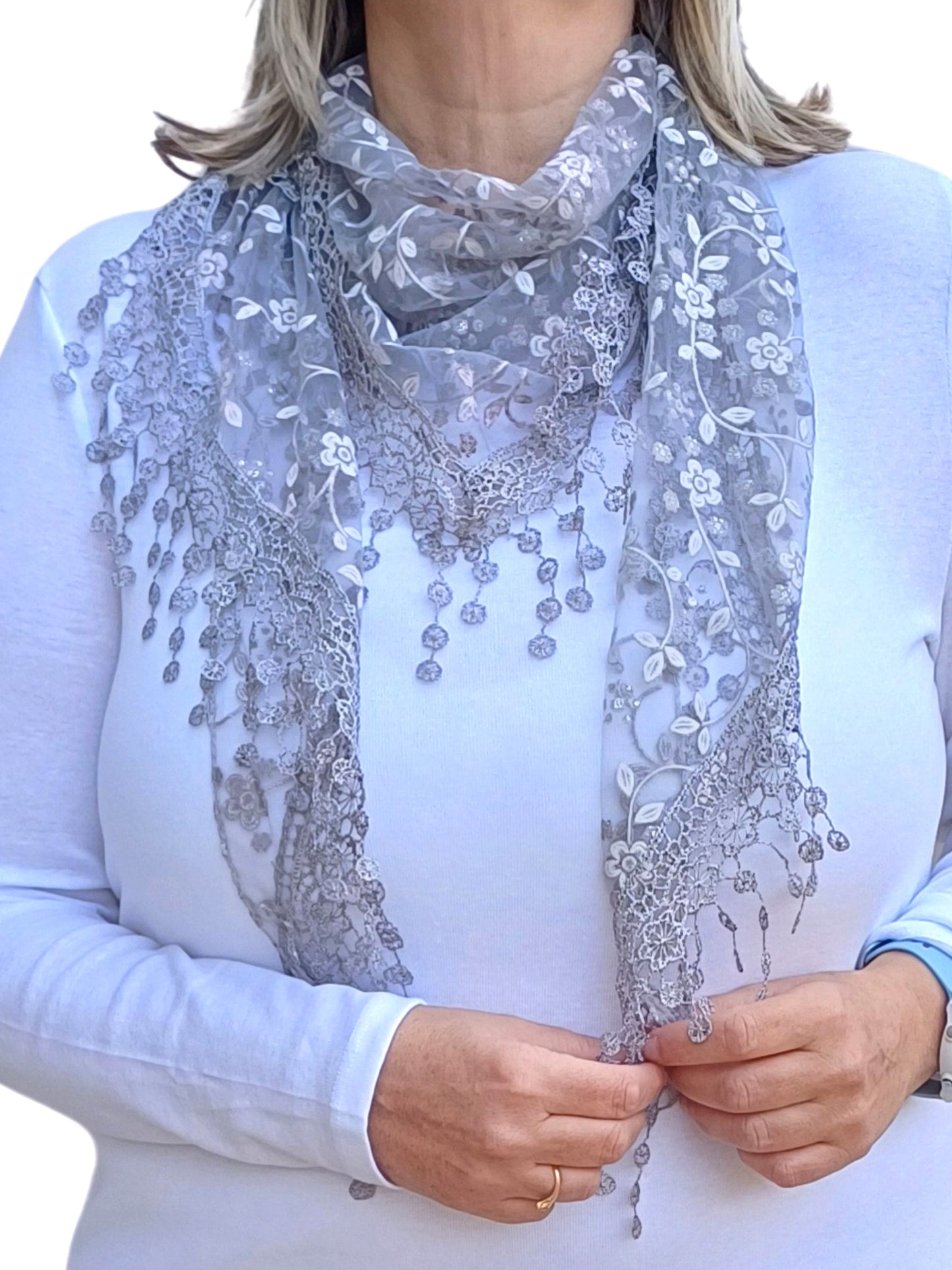 Aurora's Array Glitter Triangle Scarf with Lace & Embroidery: A woman models a light grey, sheer triangle scarf with a delicate white floral print, intricate lace trim, and dangling embroidered accents.