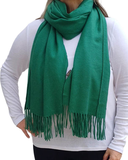 Aurora's Array: Woman models a soft, warm emerald green wool blend scarf with fringed edges, draped around her neck and shoulders.