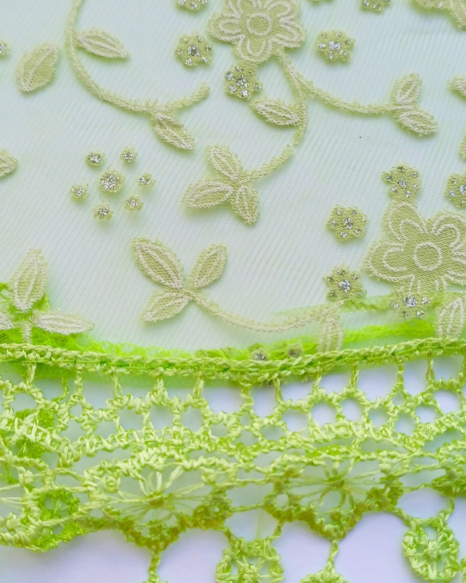 Aurora's Array Glitter Triangle Scarf with Lace & Embroidery (Close-up): A detailed close-up of a pale green, sheer fabric with delicate light green floral embroidery accented with subtle glitter. The edge features intricate bright green lace trim with da