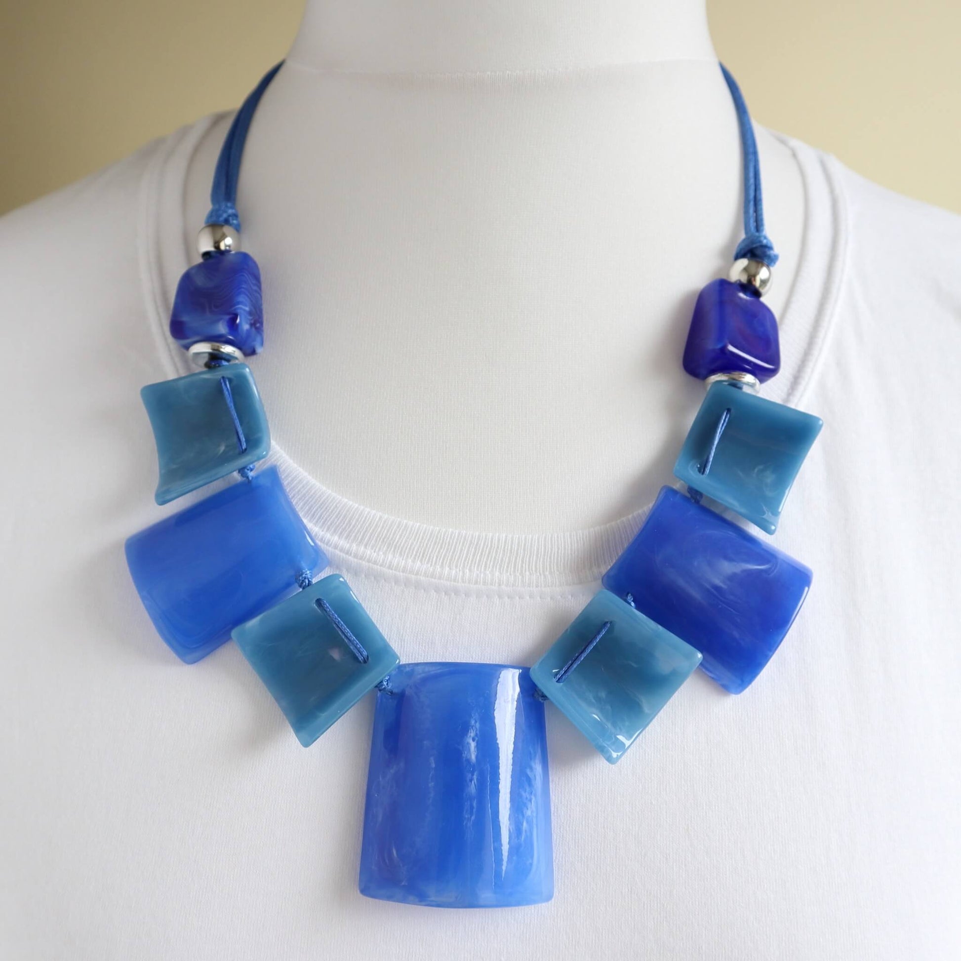 Striking statement necklace with glossy blue and light blue square and rectangular beads. Strung on a royal blue cord with silver-tone accents.
