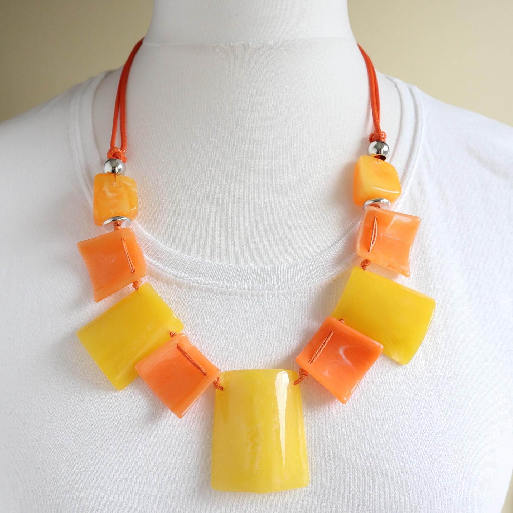 Vibrant statement necklace with glossy yellow and orange square and rectangular beads. Strung on a bright orange cord with silver-tone details.