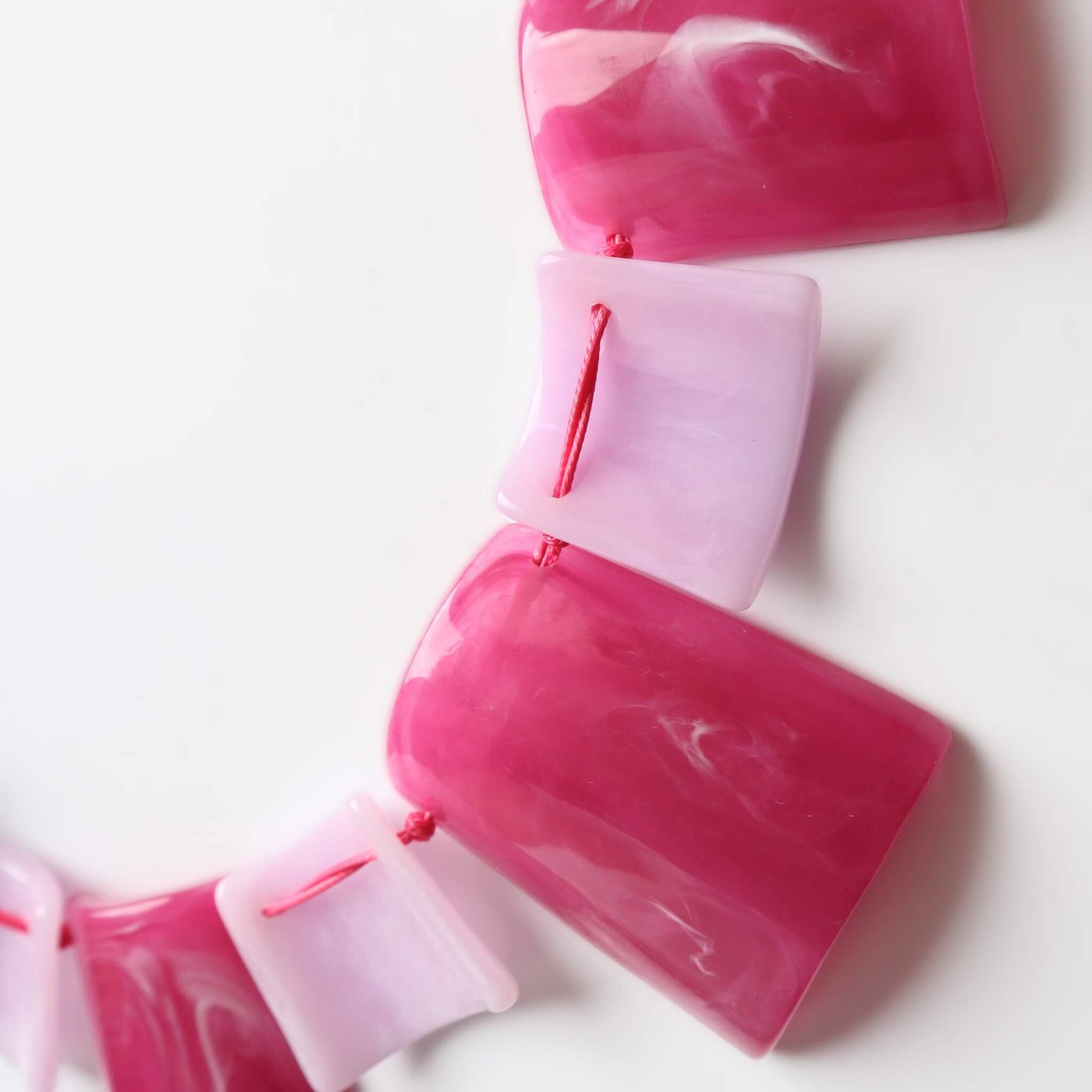 Close-up of a statement necklace featuring glossy pink and light pink marble square and rectangular beads. Strung with bright pink thread.
