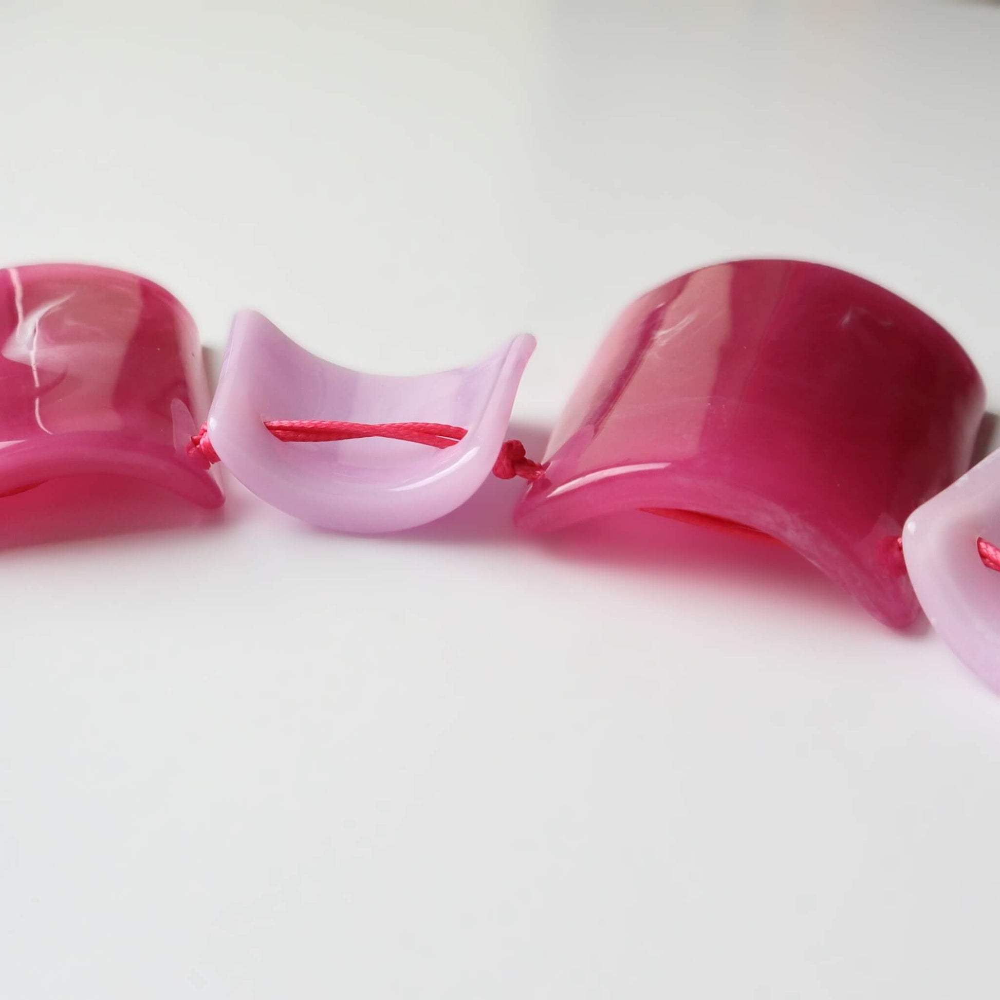 Detailed view of a statement necklace with glossy pink and light pink curved rectangular beads. Strung with bright pink thread.