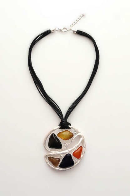 Abstract statement necklace with black cords and a silver-tone geometric pendant. Features colourful resin details and small clear stones. Unique design.