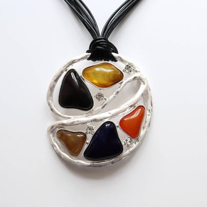 Geometric statement necklace with black cords. Features colourful resin pieces and small clear stones in a textured silver-tone abstract design.