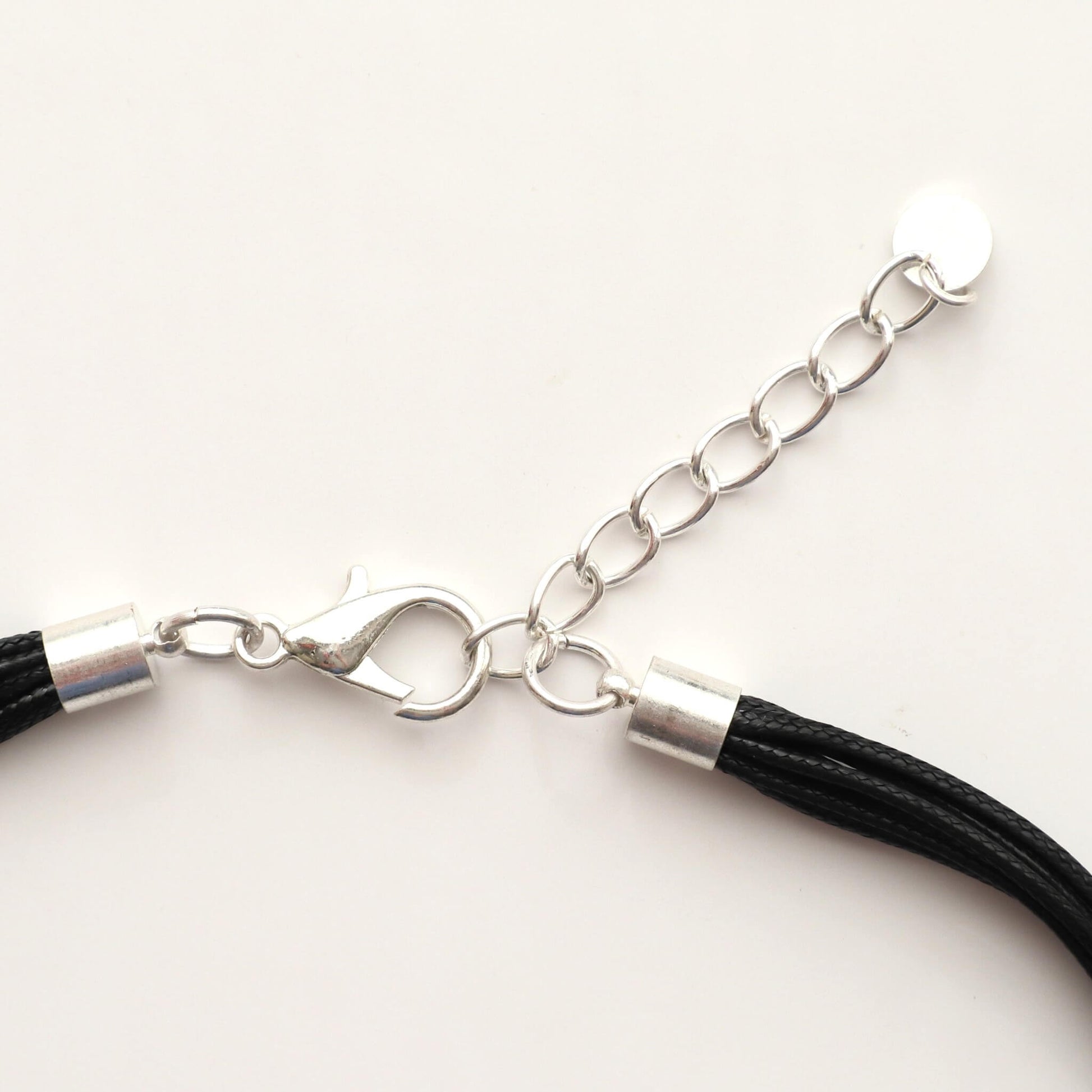 Close-up of a silver-toned statement necklace clasp and extender chain. Features a lobster claw closure and a small circular charm. Black cords are visible