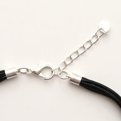 Close-up of a silver-toned statement necklace clasp and extender chain. Features a lobster claw closure and a small circular charm. Black cords are visible