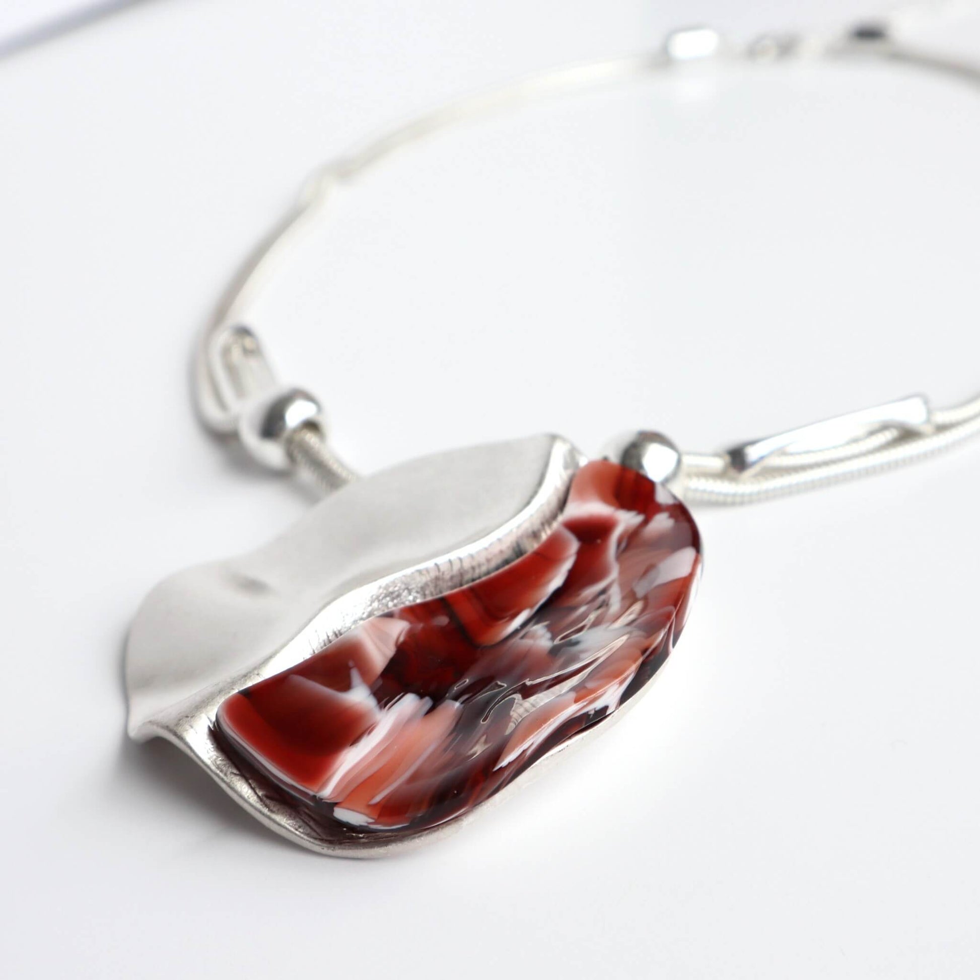 Silver-toned necklace with a unique, wavy pendant. One side is smooth, polished silver, the other has a swirling red and white pattern.