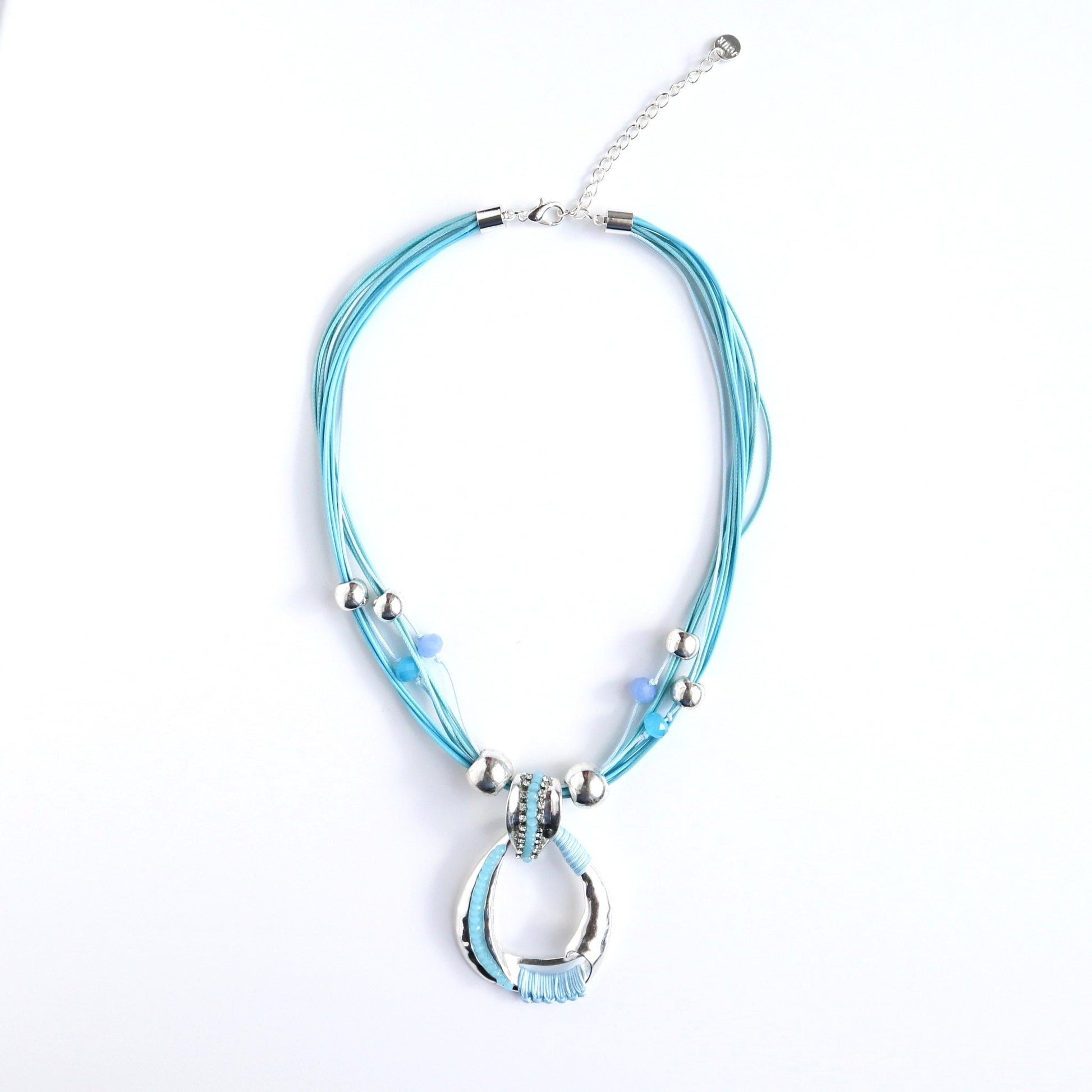 Teal cord necklace with a silver abstract oval pendant detailed with clear and teal crystals and wrapped teal thread. Silver beads accent the cords.