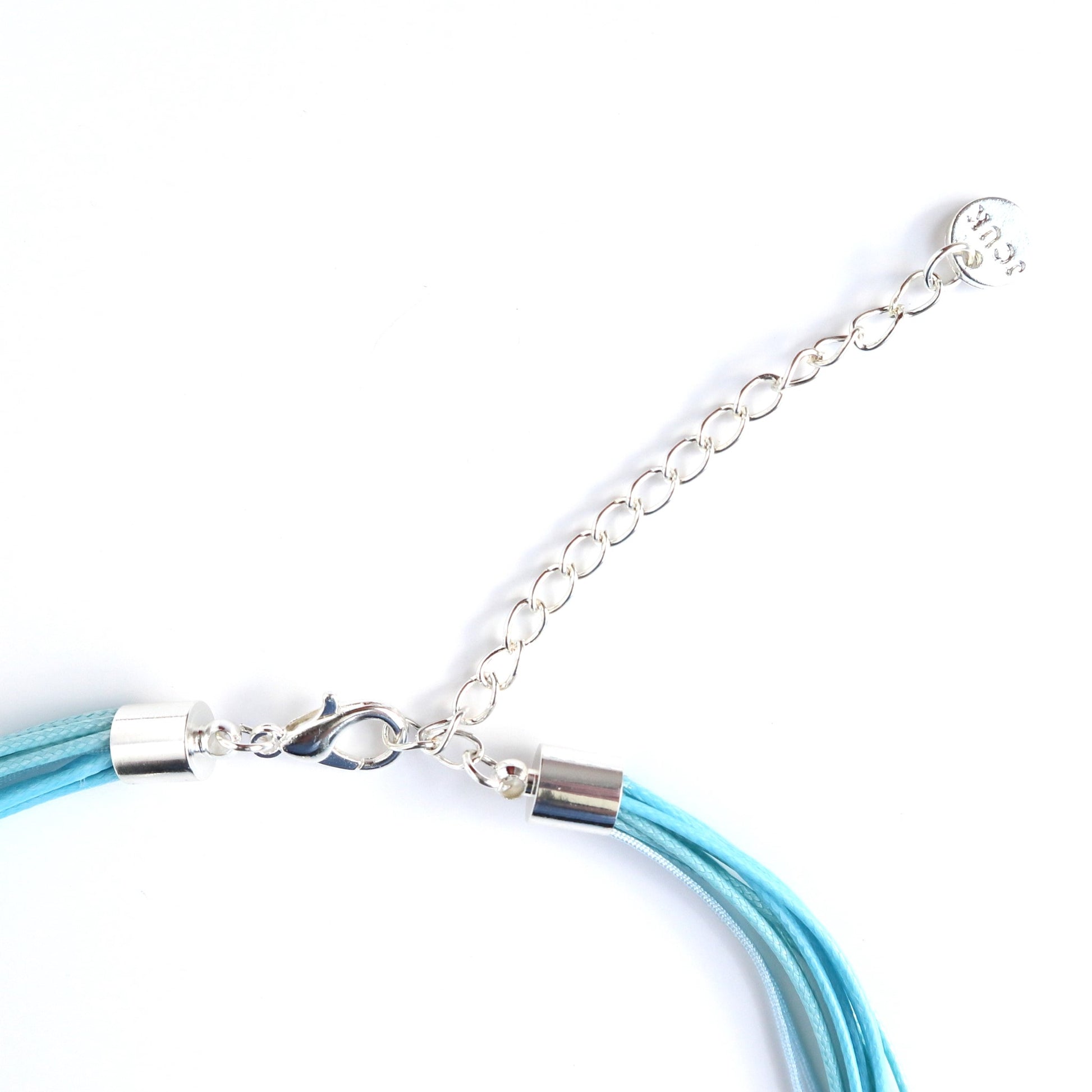 Close-up of a teal cord necklace clasp and extender chain in silver-tone metal. Multiple cords are secured with silver caps.