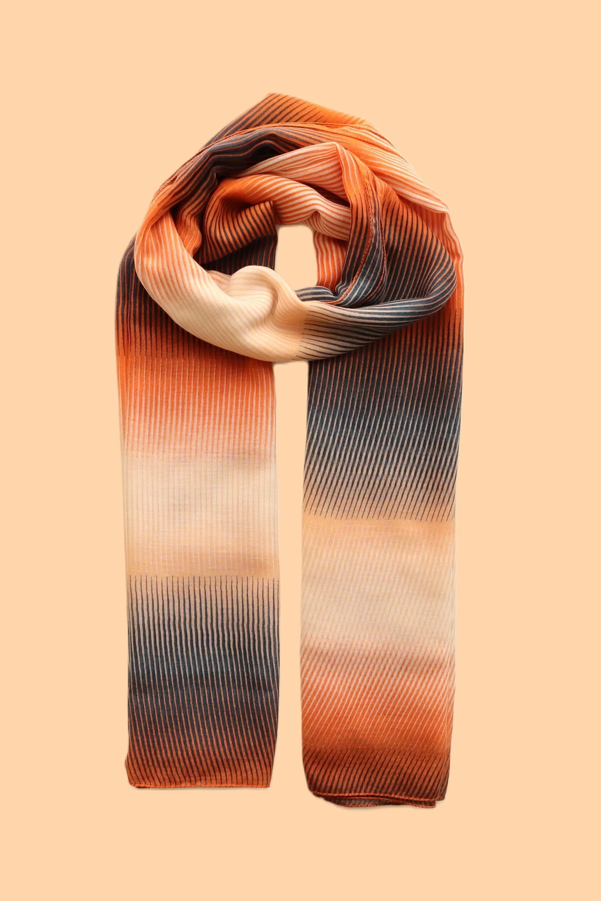 Lightweight scarf featuring a flowing striped texture with an ombre transition of dark grey, bright orange, and soft cream hues.