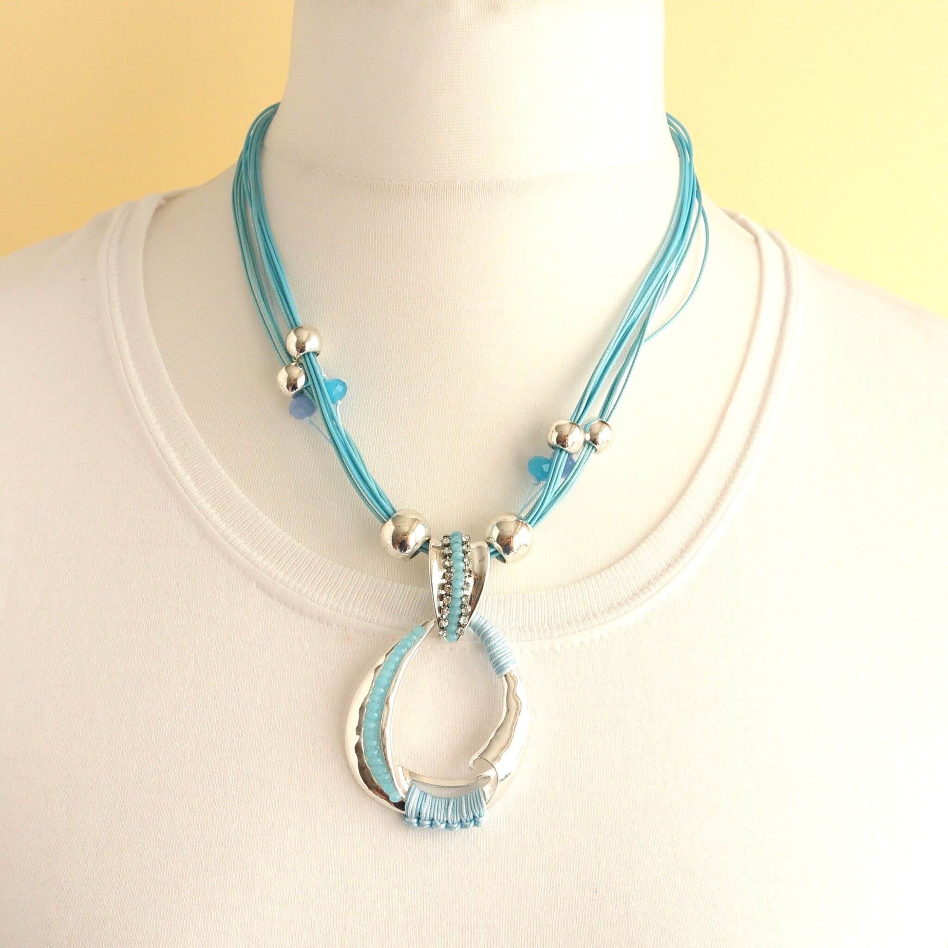 Teal cord necklace with a silver abstract oval pendant featuring embedded clear and teal crystals and wrapped teal thread.