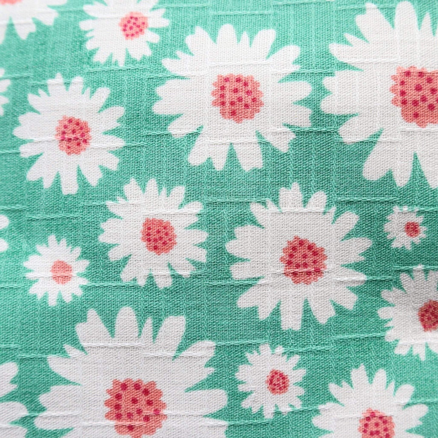 Close-up of a mint green fabric with a repeating pattern of white daisies with textured pink centers.