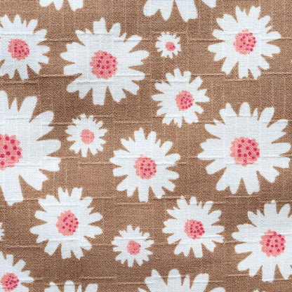 Detailed view of a light brown fabric displaying a repeating pattern of white daisies with textured pink centers.