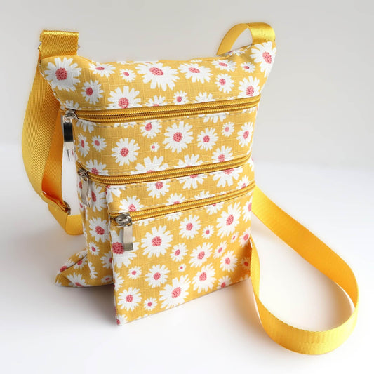 Yellow crossbody bag with a white and pink daisy print. Features three zippered compartments and a bright yellow adjustable strap.