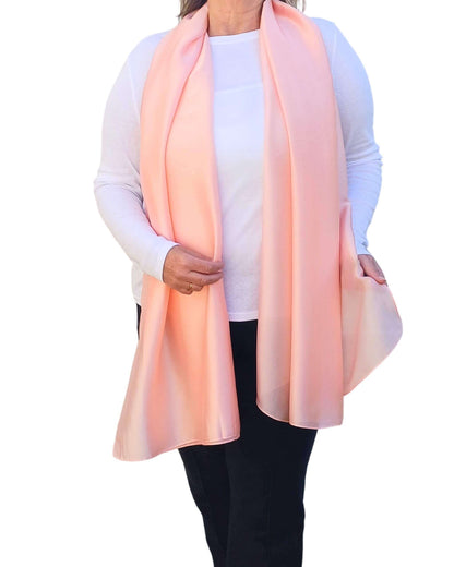 Aurora's Array Elegant Satin Shawl: Woman models a soft, peach-coloured pink silky shawl draped over a white top.