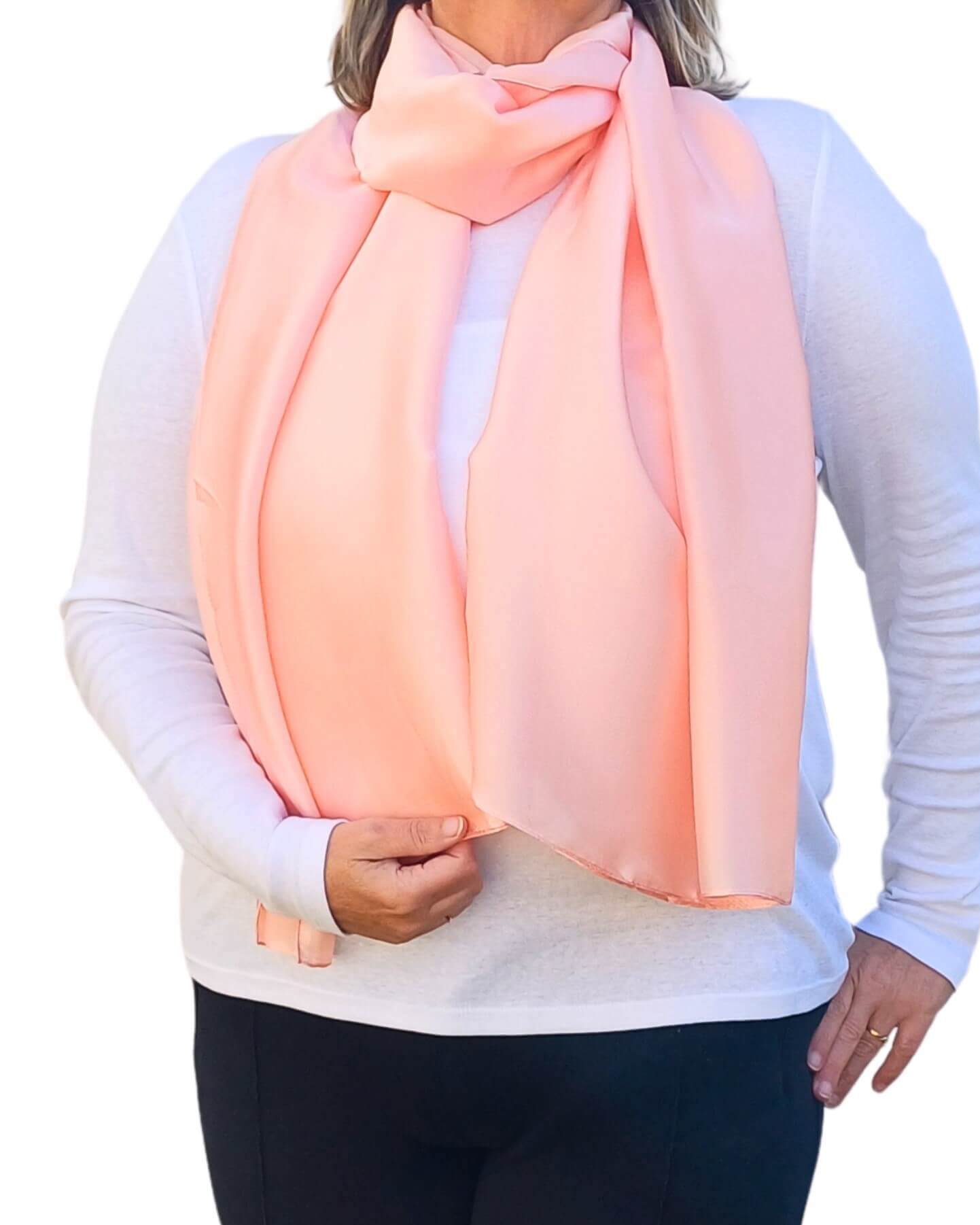 Aurora's Array Elegant Satin Shawl: Woman models a soft, peach-colooured pink silky scarf wrapped around her neck over a white top.