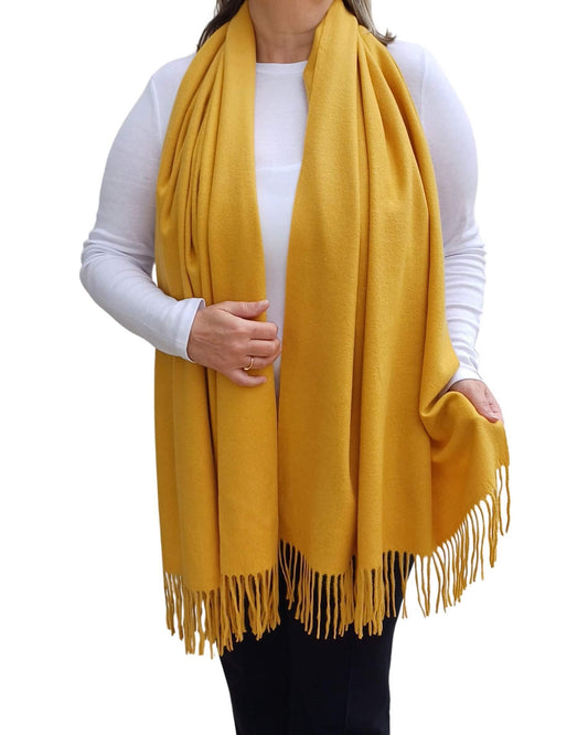 Aurora's Array: Woman models a soft, warm mustard yellow wool blend scarf with fringed edges, draped around her neck and shoulders.