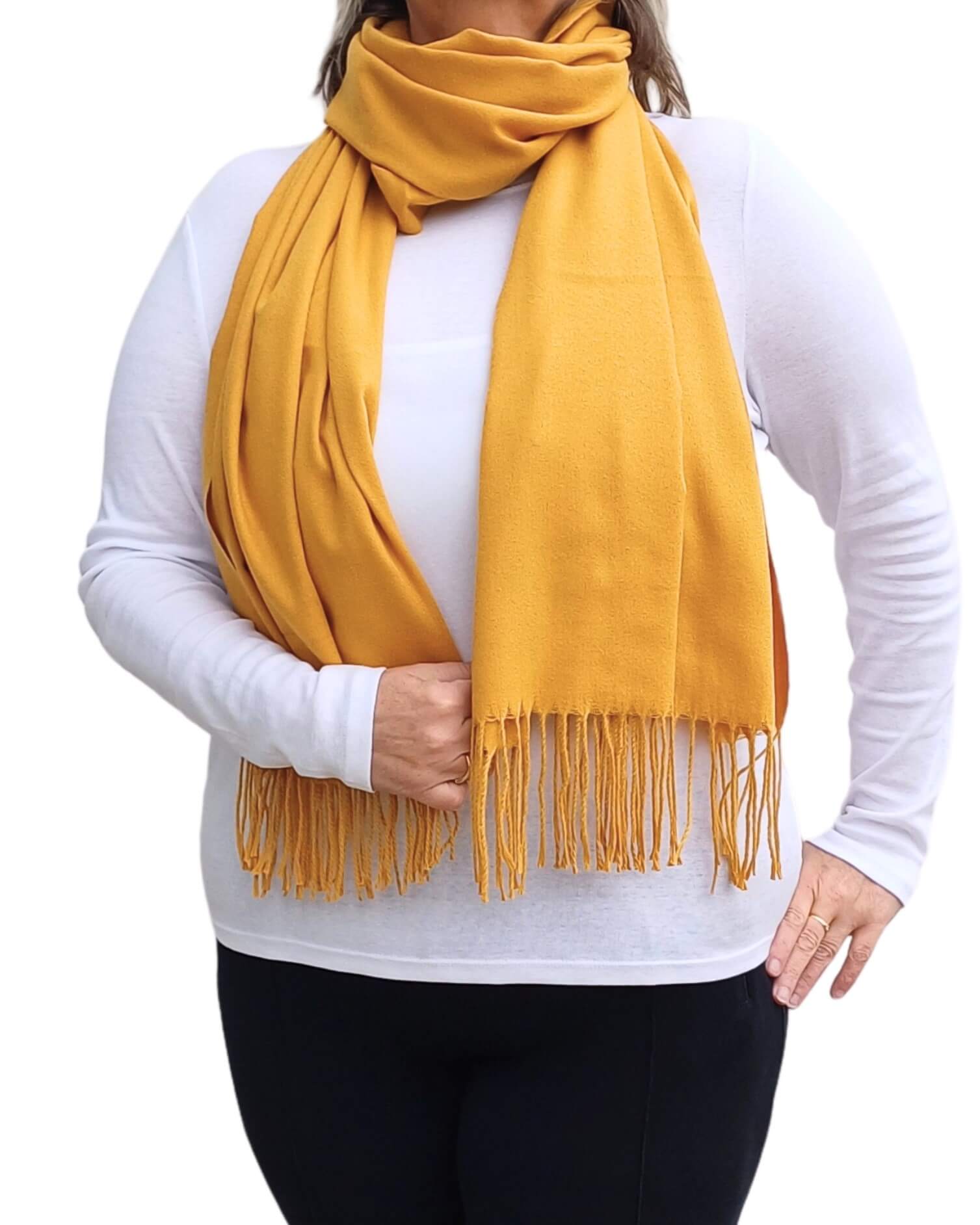 Aurora's Array: Woman models a soft, warm mustard yellow wool blend scarf with fringed edges, wrapped around her neck.