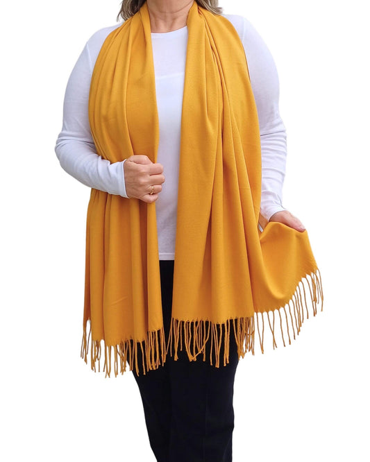 Aurora's Array: Woman models a soft, warm mustard yellow wool blend scarf with fringed edges, wrapped around her neck.