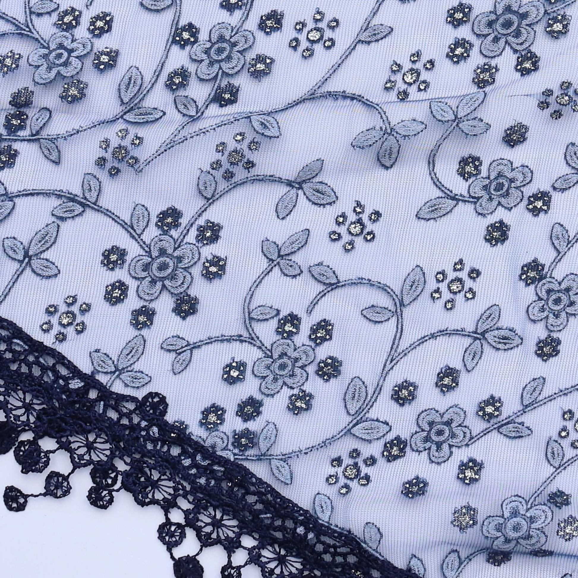 Aurora's Array Glitter Triangle Scarf with Lace & Embroidery (Close-up): A detailed close-up of a dark blue, sheer fabric with delicate white floral embroidery accented with subtle glitter. The edge features intricate dark blue lace trim with dangling emb