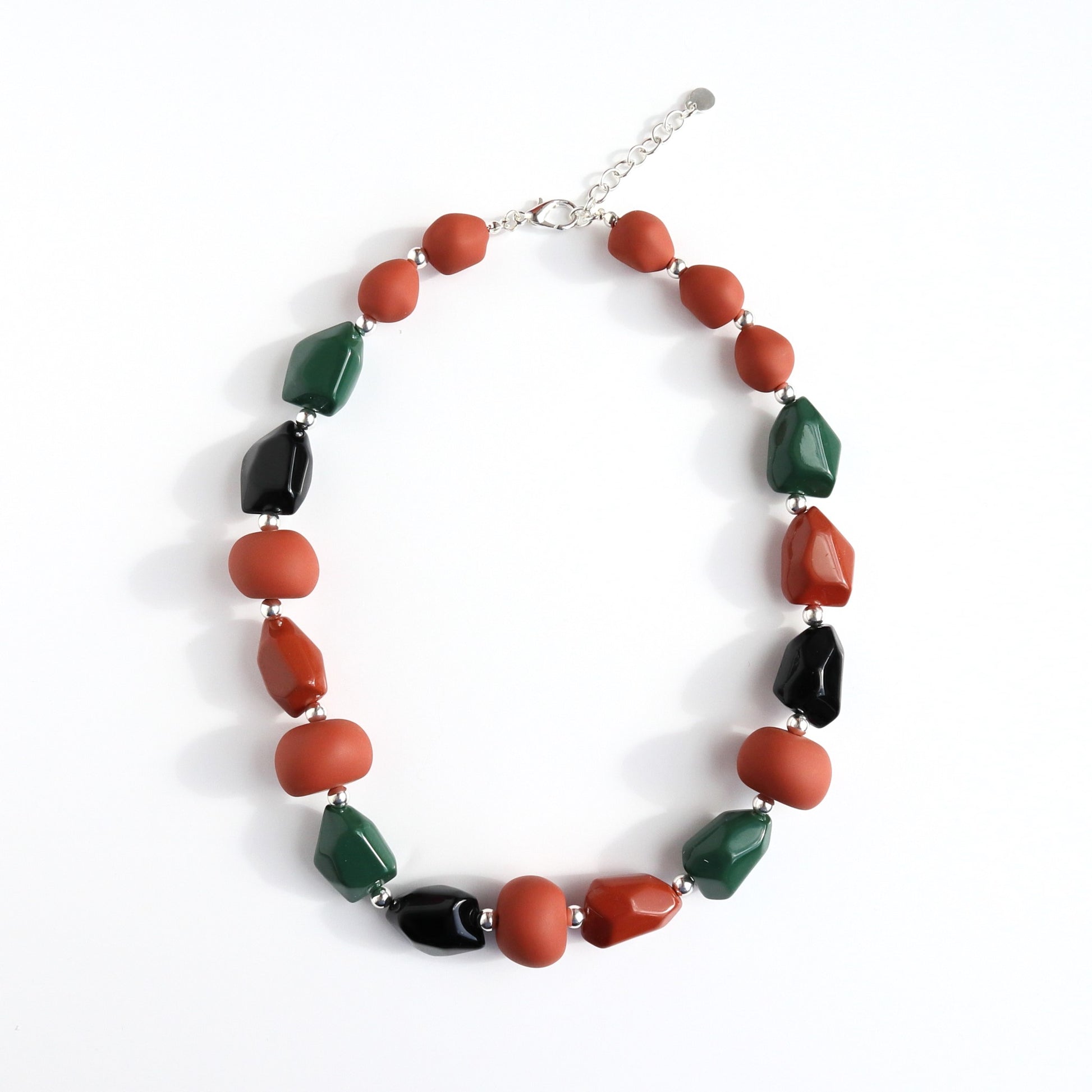 Short beaded necklace with matte rust-orange, shiny black, and glossy dark green irregular beads, separated by small silver-tone spacers. Silver-tone clasp.