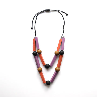 Bold, geometric necklace with black cord, featuring matte lavender and orange rectangular wooden beads, and smooth tan and black round wooden beads.