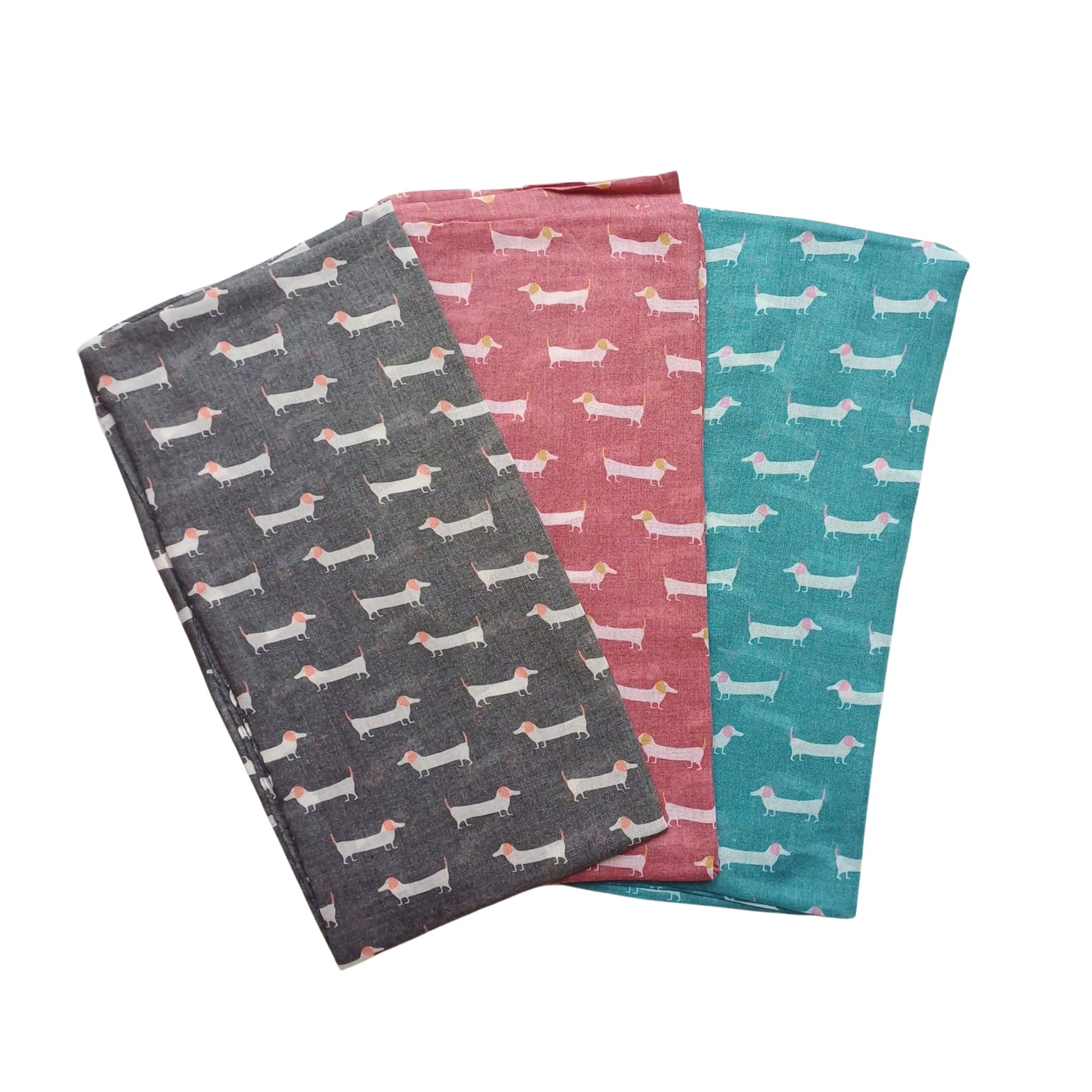 Three sausage dog scarves in charcoal, deep red and teal laid side by side on white background