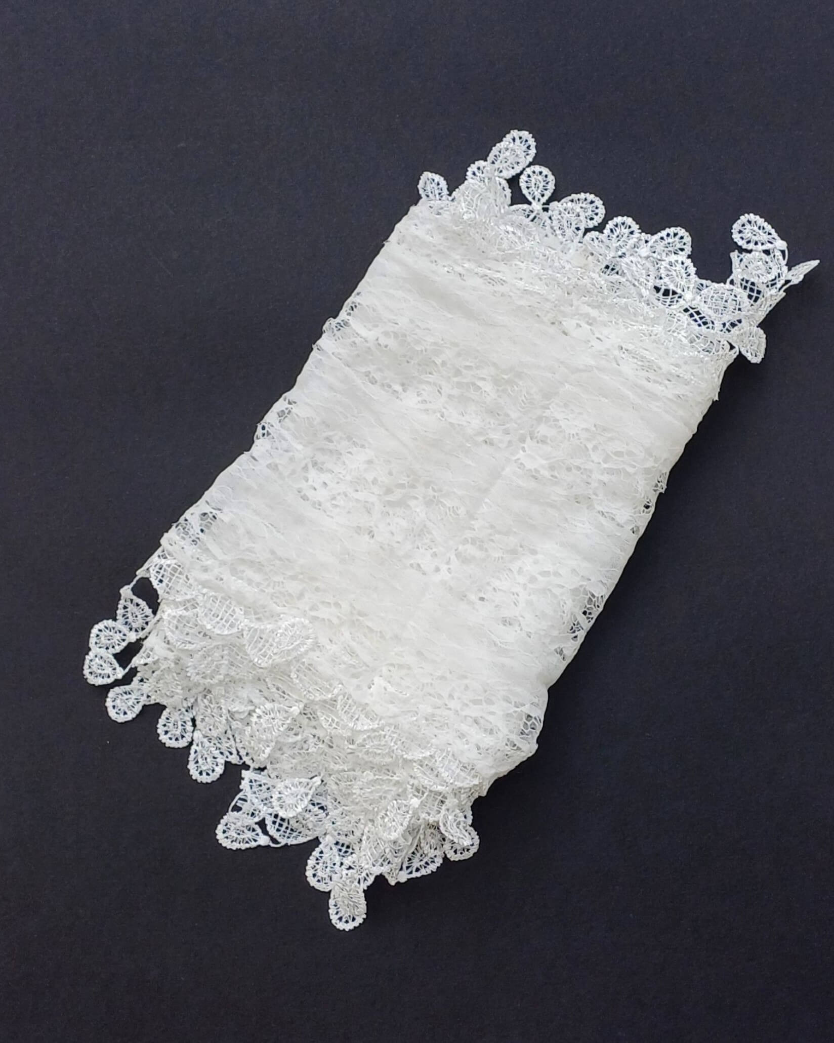 Aurora's Array: A delicate white lace scarf, folded to show its intricate floral pattern and scalloped edges.