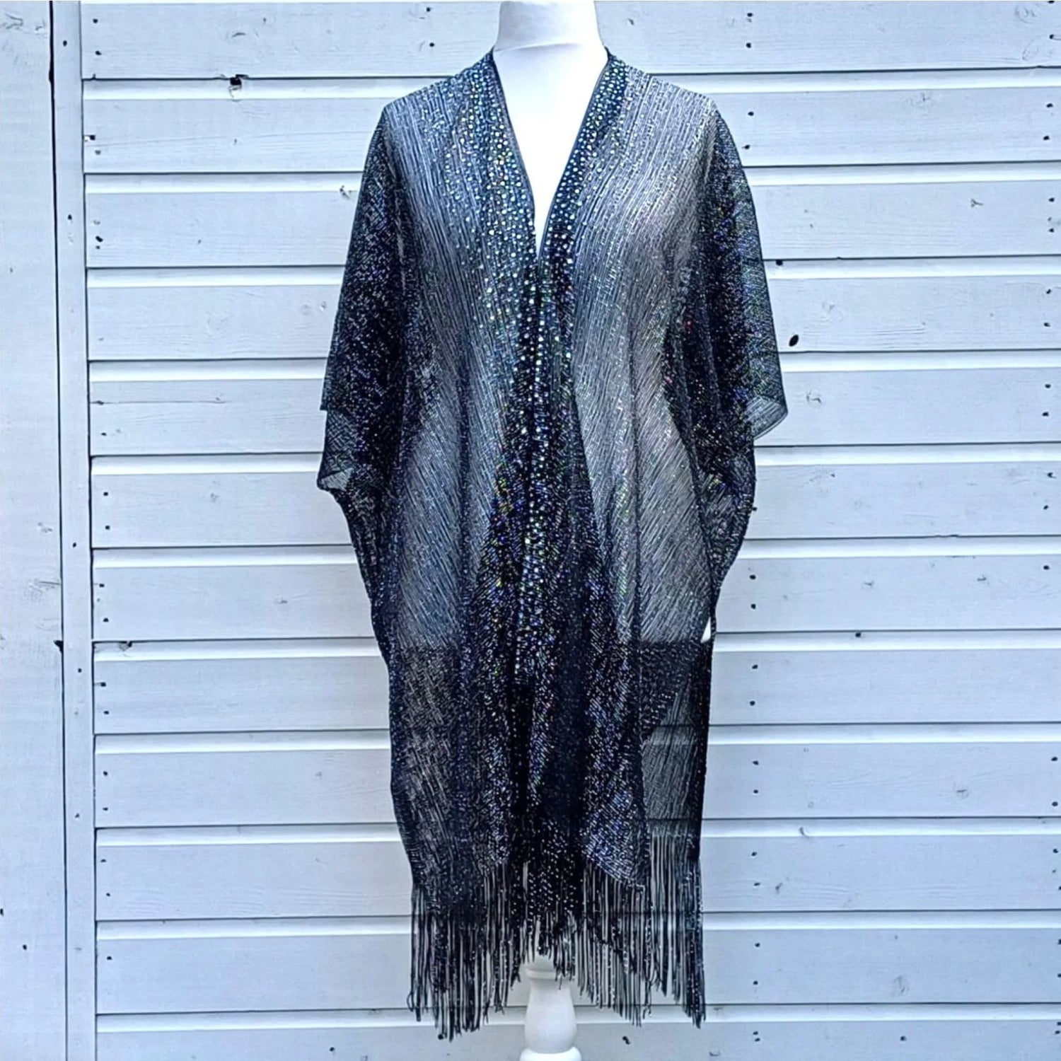 Black fringe garment on a mannequin against a white wooden panel background