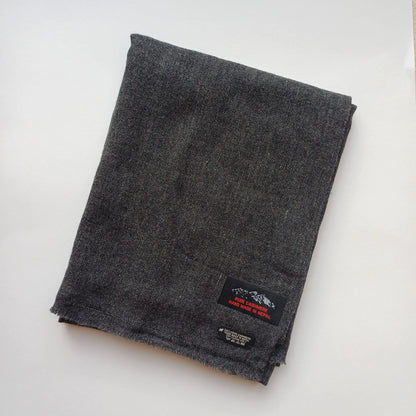 Charcoal grey cashmere scarf folded neatly showing brand label on a white background unisex winter accessory handmade in Nepal
