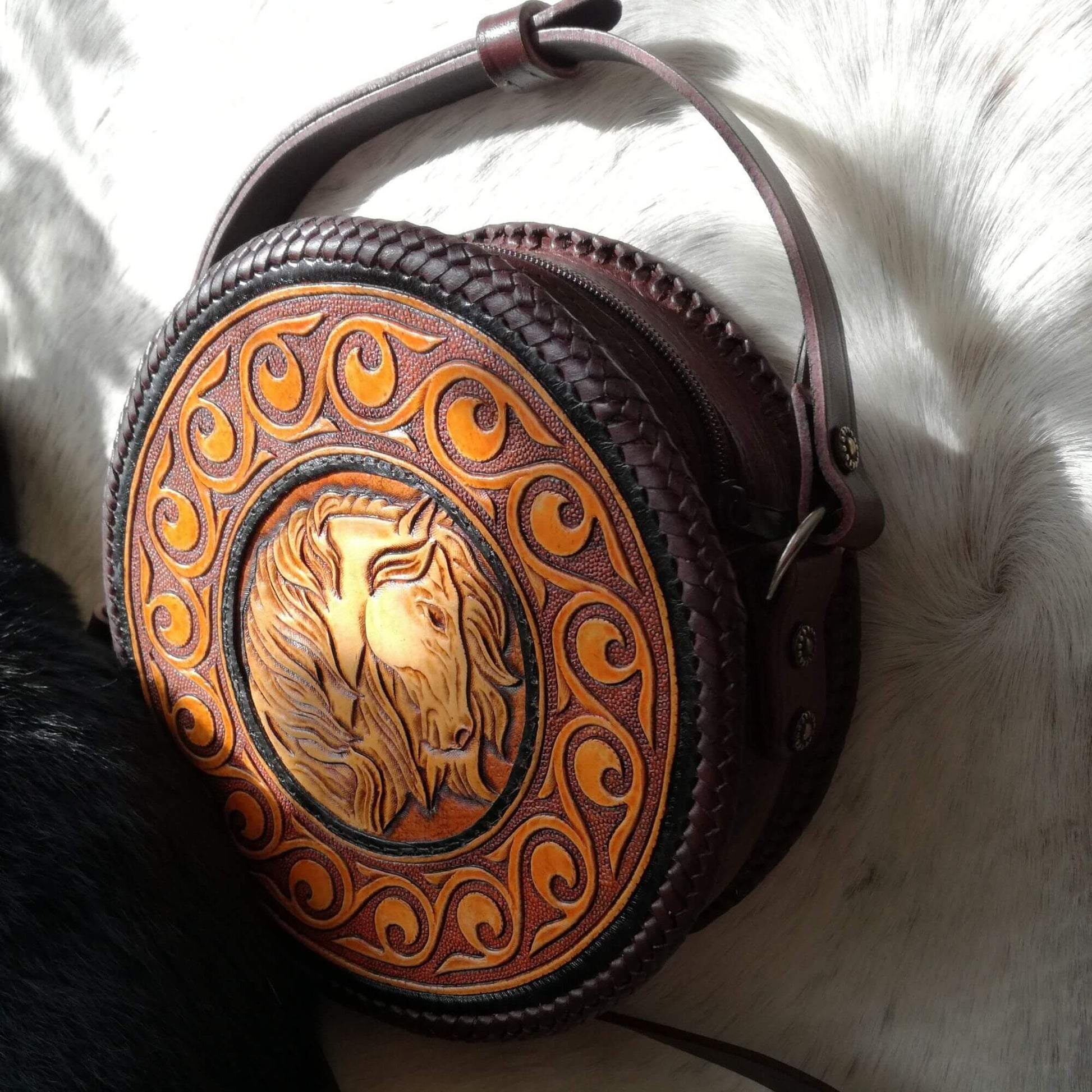 Angled front view of round leather crossbody bag with hand-tooled horse design – Equina