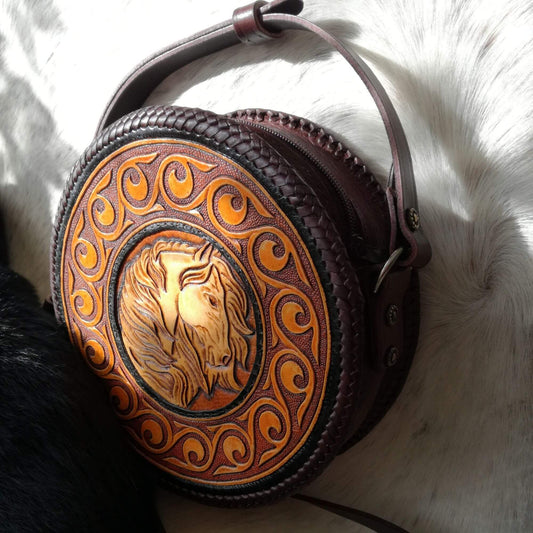 Angled front view of round leather crossbody bag with hand-tooled horse design – Equina