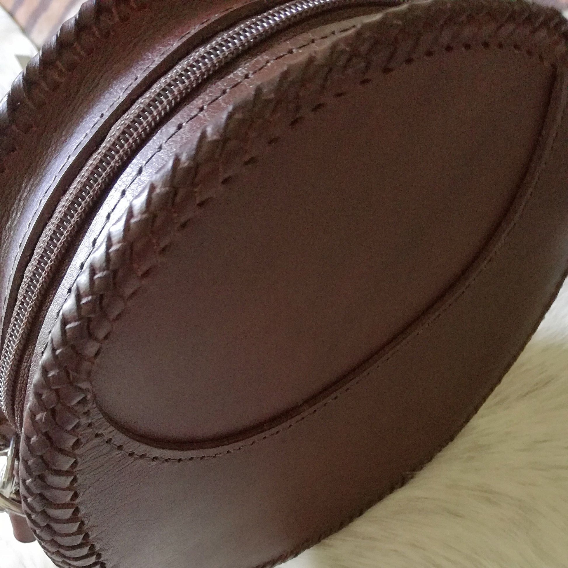 Back view of handmade round leather bag with smooth finish and laced edges