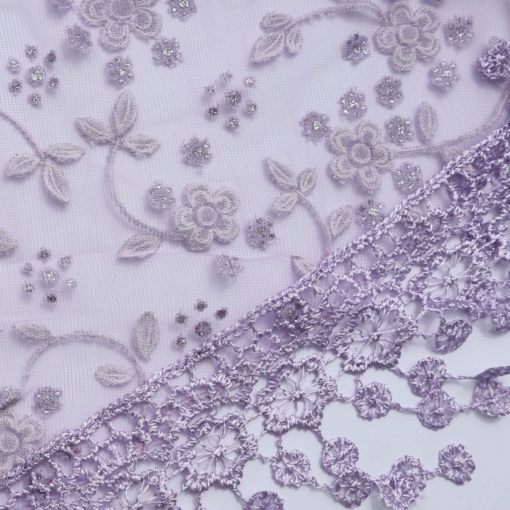 Close up of the Auroras Array Glitter Triangle Scarf in lilac showing floral lace embroidery and glitter detail on sheer fabric