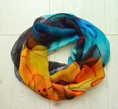 Bright chiffon scarf with vivid flower print in orange, yellow and blue tones laid flat
