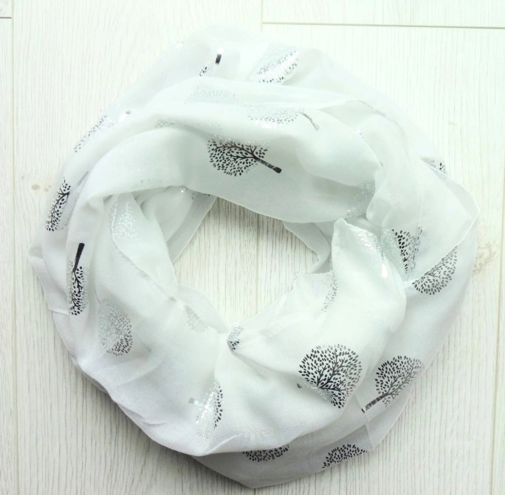 White scarf with silver foil tree of life patterns on a light wooden surface placed in a circle